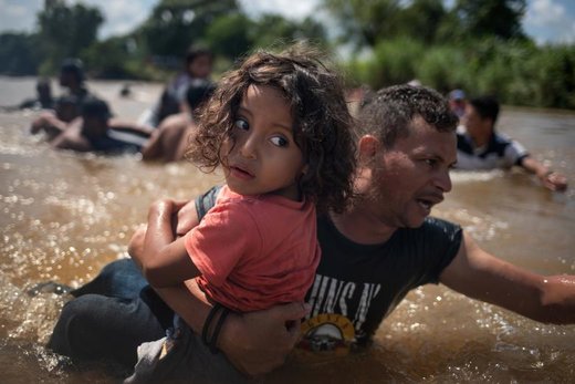 یک مهاجر هندوراسی با کاروان مهاجران آمریکای مرکزی در حالی که فرزندش را در آغوش گرفته از رودخانه عبور می کند