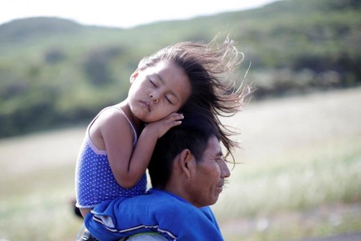مهاجر گواتمالایی که جزء کاروان مهاجران آمریکایی است در حالی که دخترش را روی دوش خود گذاشته در یکی از بزرگراه‌های مکزیک به سوی آمریکا می‌رود