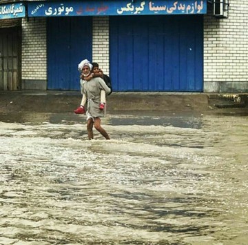 پدبزرگ اهوازی در حال جابجایی نوه دانش آموزش در منطقه علوی اهواز بعد از بارندگی بامداد امروز