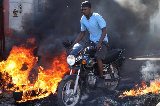 یک مرد با موتورسیکلت در زمان اعتصاب عمومی در شهرپورتو پرنس پایتخت هائیتی از میان آتش عبور می‌کند