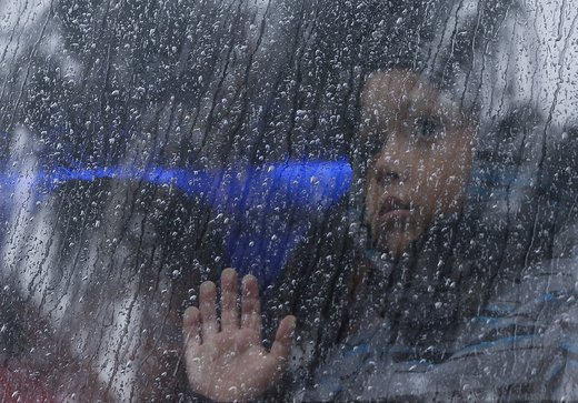 یک کودک از پشت پنجره اتوبوس در شهر تیخوانا مکزیک به بیرون نگاه می کند در حالی که هوا بارانی است