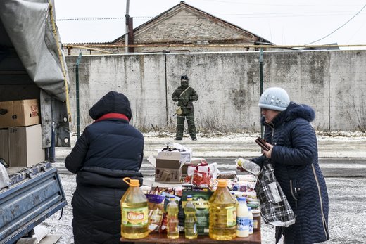 نگهبان مرزی روسیه در پشت سیم خاردار در مرز این کشور با اوکراین ایستاده در حالی که مردم خرید می‌کنند