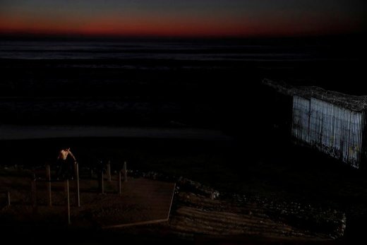 یک مرد در گرگ و میش ساحل کنار حصار مرزی ایالات متحده در ایالت تیخوانا مکزیک کار می کند