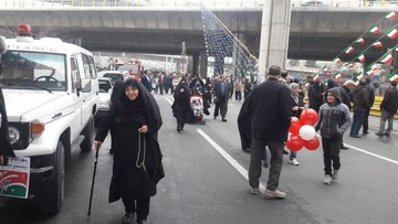 با انکه پایش درد می‌کند خود را با عصا به میان مردم رسانده است تا در جشن چهل سالگی انقلابش شرکت کند