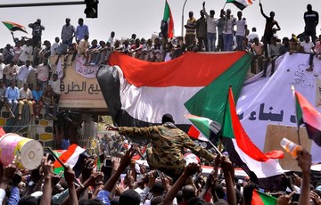 بعد از اینکه عمرالبشیر، رئیس‌جمهور سودان، توسط نیروهای امنیتی بازداشت شد، یک افسر ارتشی در میان جمعیت در خارطوم، پرچم ملی کشورش را به دست گرفته است
