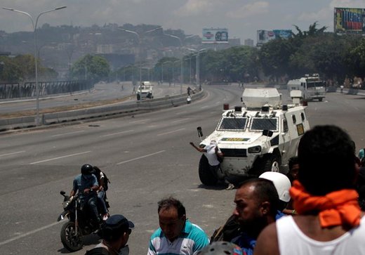 یک تظاهرکننده مخالف دولت ونزوئلا مقابل خودروی نظامی این کشور در نزدیکی پایگاه هوایی در شهر کاراکاس ایستاده است