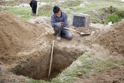 تشلی بکه 65 ساله، در حال استراحت کنار قبری است که برای مراسم تدفین در قبرستان قوش‌تپه شهر آق‌قلا آماده کرده است
