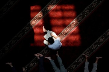 یک مسلمان در مسجدی در شهر جاکارتا اندونزی قرآن می‌خواند، در حالی که دیگران در حال استراحت هستند