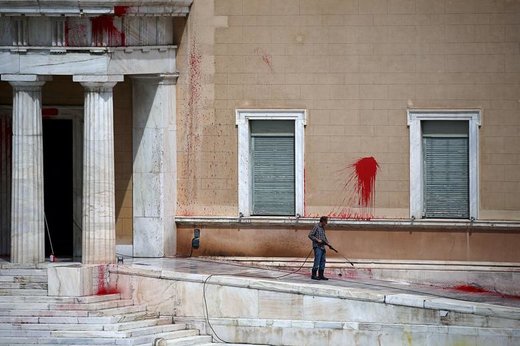 یک کارگر رنگ‌های پرتاب شده به سوی نمای ساختمان مجلس یونان توسط مهاجمان ناشناس را در شهر آتن پاک می‌کند