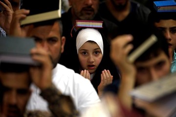 یک دختر شیعه عراقی  در ماه مبارک رمضان در حرم امام علی(ع) شهر نجف عراق، قرآن کریم را بر روی سر خود قرار داده است