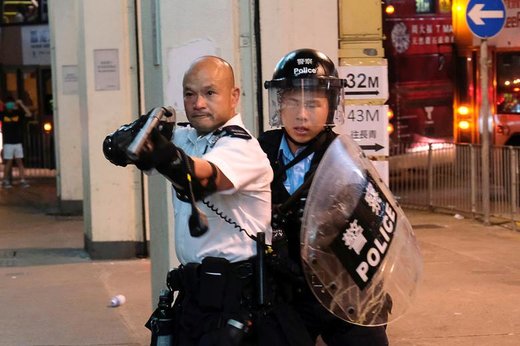 یک افسر پلیس هنگ‌کنگ تفنگ را به سوی معترضان به لایحه استرداد مجرمان قضایی به چین گرفته که ایستگاه پلیس را به محاصره درآورده‌اند