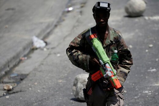 یک مرد با اسلحه اسباب‌بازی در اعتصاب عمومی علیه کمبود سوخت در پورتو پرنس  هائیتی در خیابان مسدود شده با مانع راه می‌رود