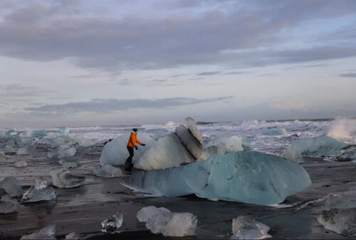 یک گردشگر در حال دست زدن به توده های یخی خرد شده در ایسلند