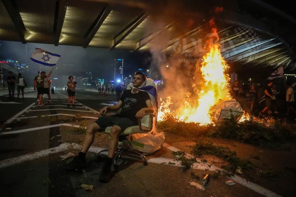 عکس | تصویر جالب یک معترض اسرائیلی در حال استراحت؛ پشت به آتش با پاهای زخمی در بزرگراه ایالون تل‌آویو
