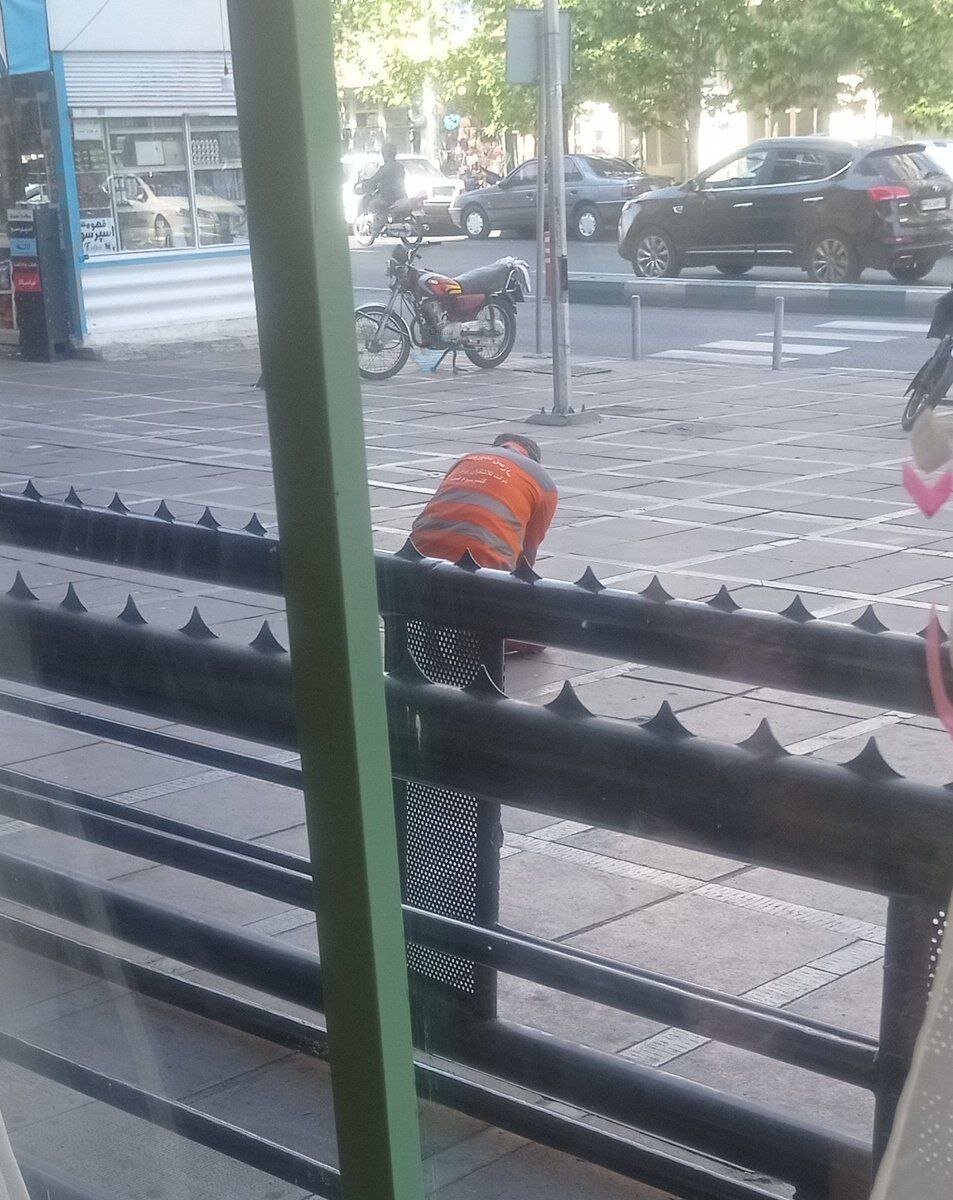 عکس | تصویر تلخ از یک پاکبان در تهران؛ نشستن چند ساعته روی زمین برای پاک کردن بروشور چسبدار از روی پیادهرو